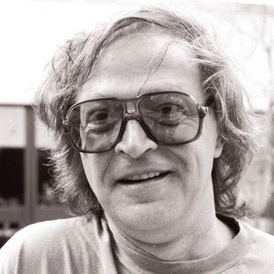 A black and white portrait of bill bissett smiling candidly.