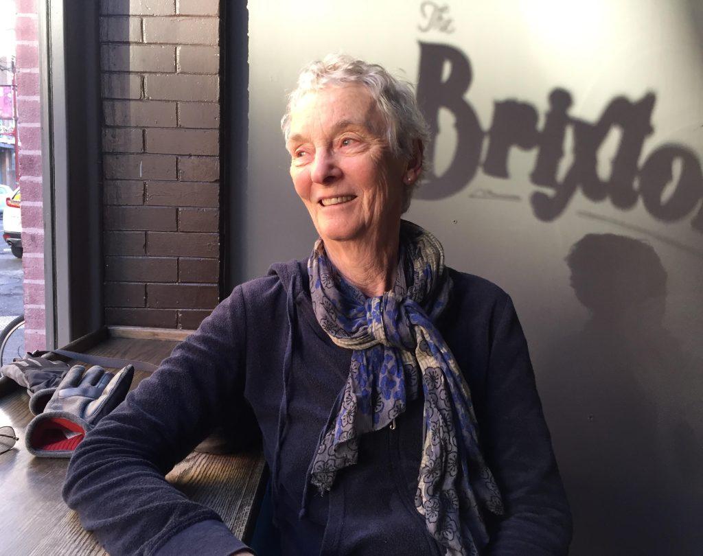 Pauline Butling sits smiling beside a window she gazes out of